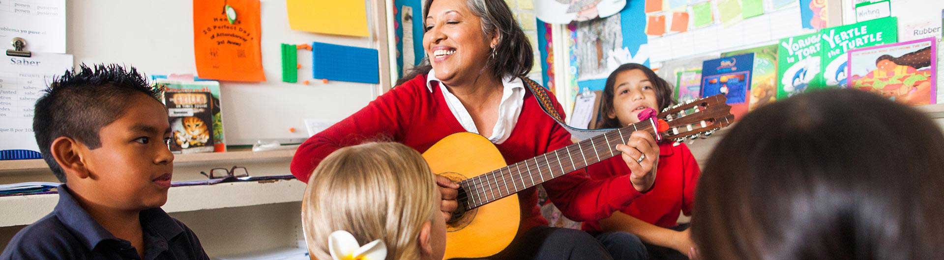 Latina teacher playing guitar in a classroom with students around her