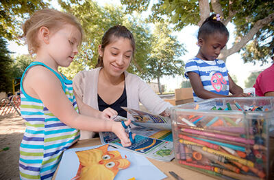 Teacher sitting at an outdoor table working on art projects with young students