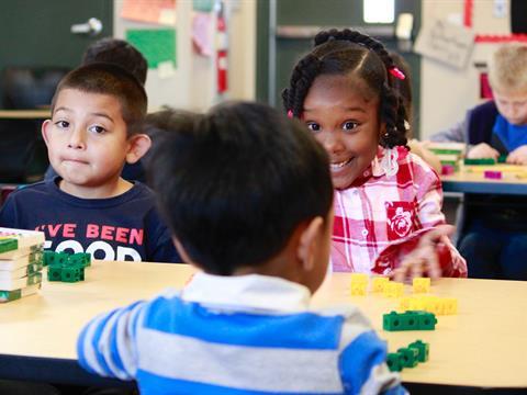 Three young students sitting together at a desk playing with building blocks