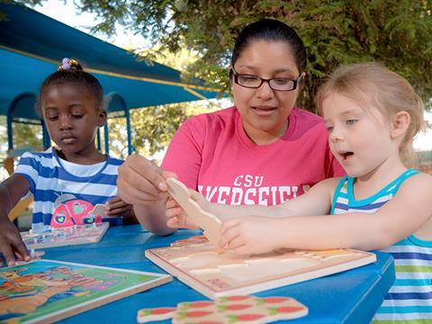 Teacher sitting down at an outside table with two young students