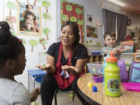 Teacher sitting at a table with two small students helping with art projects