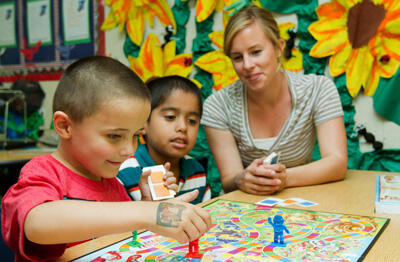 Teacher sitting at table playing a board game with two young students
